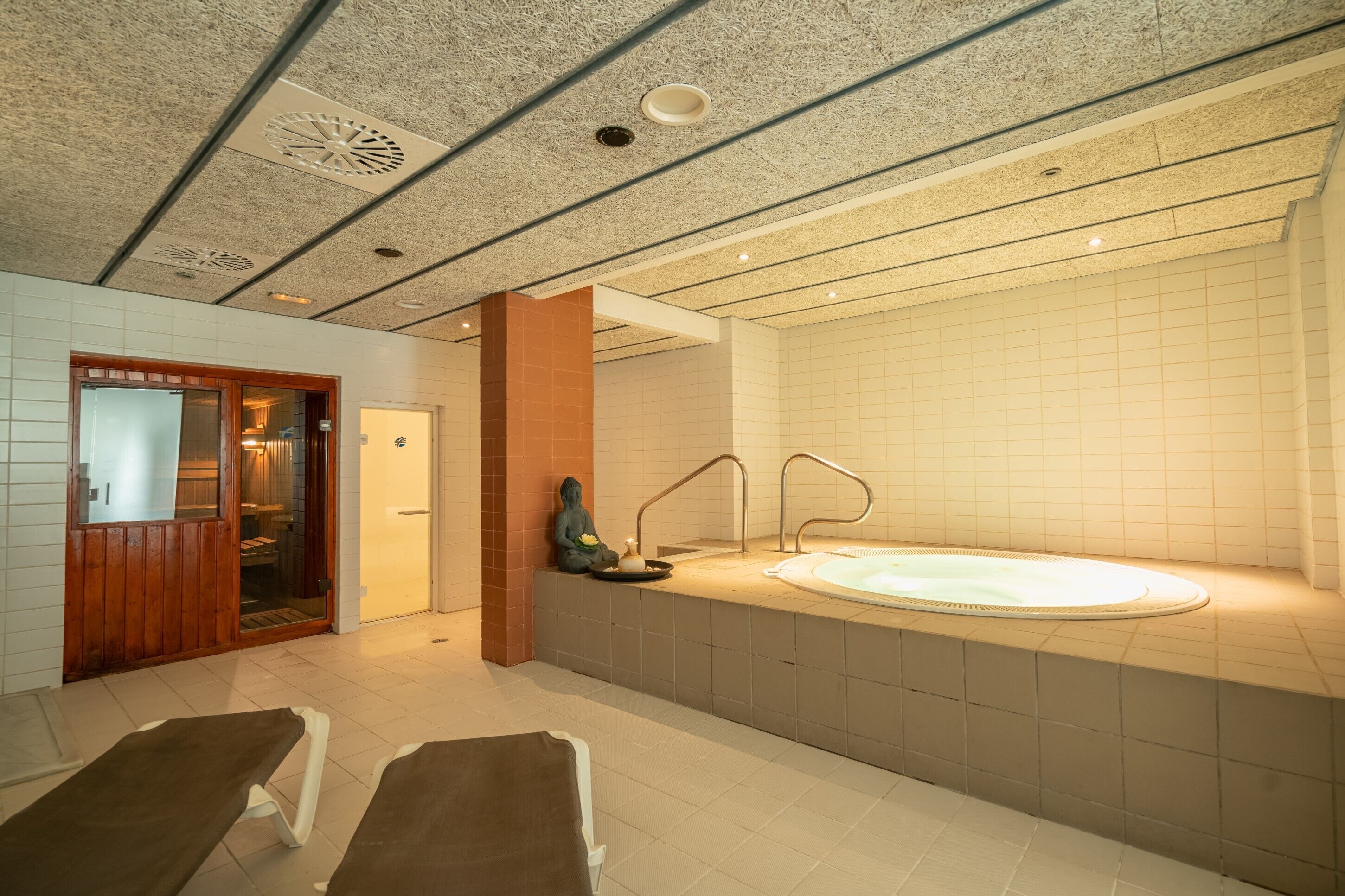 Um spa moderno com uma banheira grande, duas espreguiçadeiras e uma estátua para meditação.
