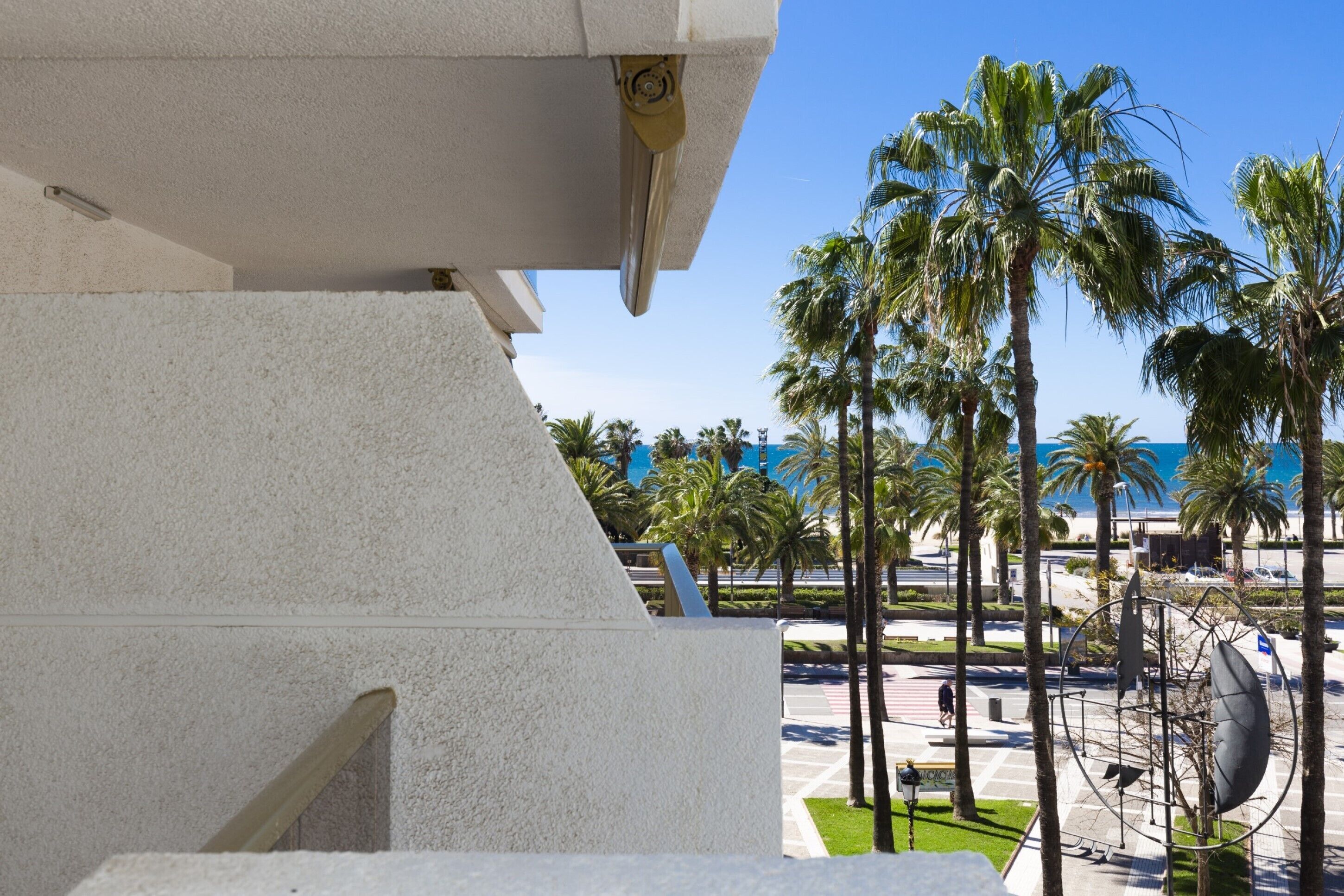 Un bâtiment moderne à l’extérieur blanc, offrant une vue sur des palmiers et un ciel bleu dégagé.