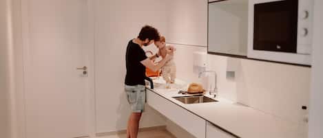 Una cocina moderna con armarios blancos, un lavamanos de acero inoxidable y un microondas.