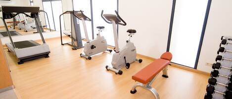 A gym with treadmills, stationary bikes, and a bench.