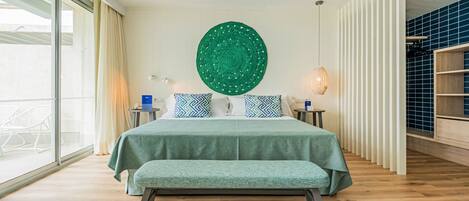 A modern bedroom with a large bed, a ceiling fan, a green wall hanging, and a view of the outdoors.