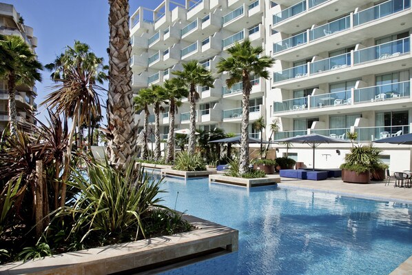 Una piscina al aire libre, sombrillas, sillones reclinables de piscina