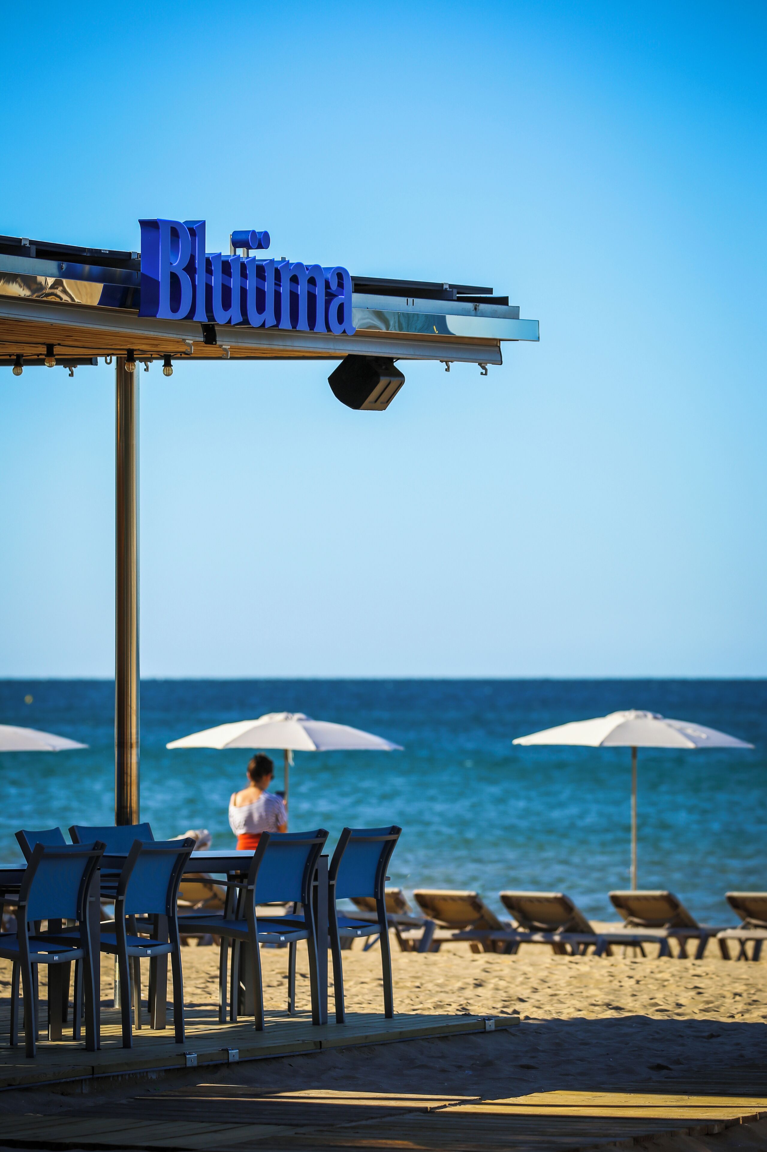 Un restaurante frente a la playa llamado "Bluuma", con terraza y sombrillas.