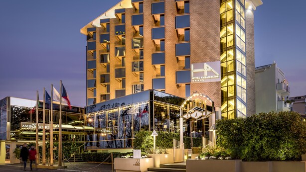 Un hotel con varios balcones, fachada de vidrio y un letrero que dice "HOTEL AMBASSADOR".