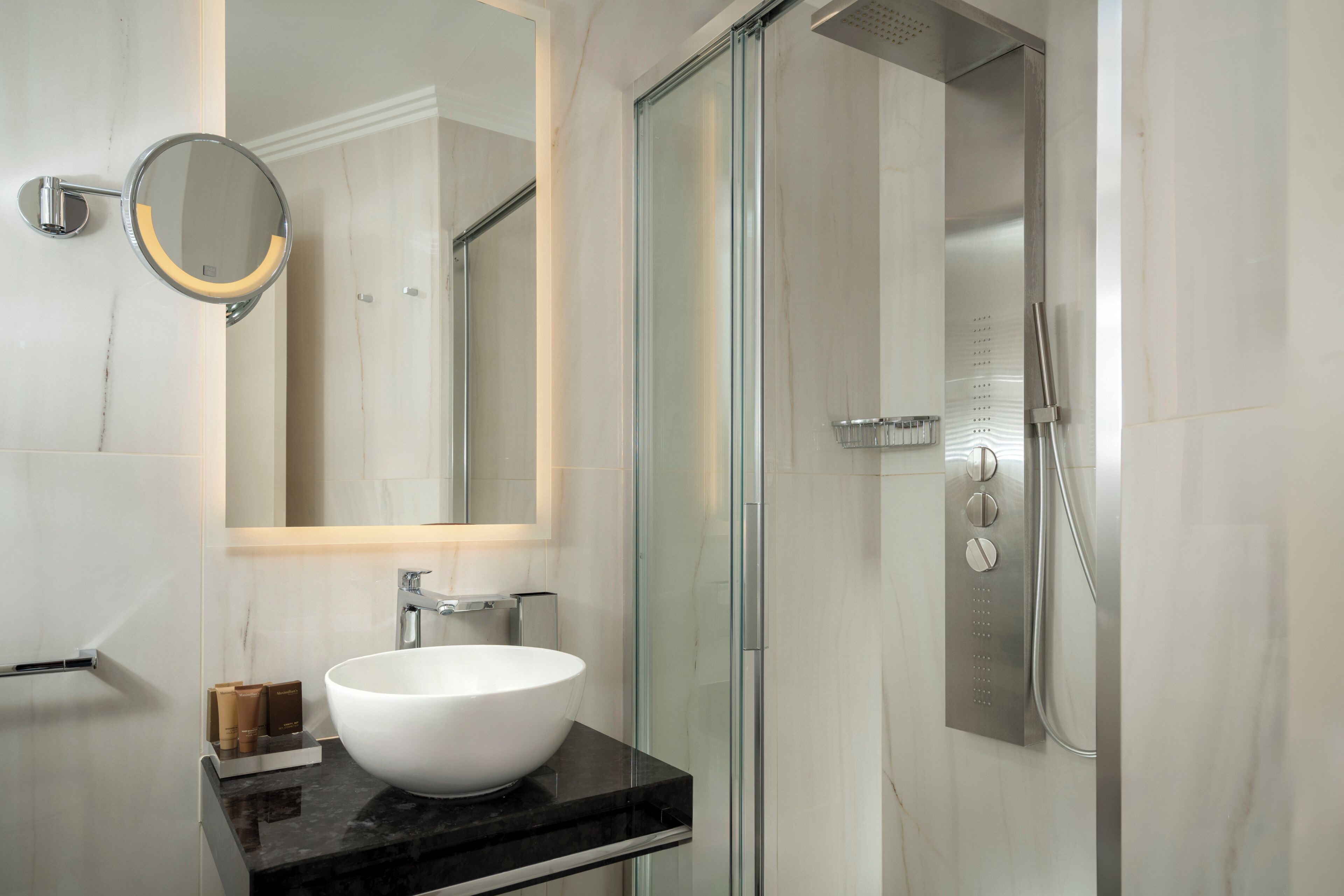 Un bagno moderno con un lavandino bianco grande, uno specchio rotondo e una cabina doccia in vetro.
