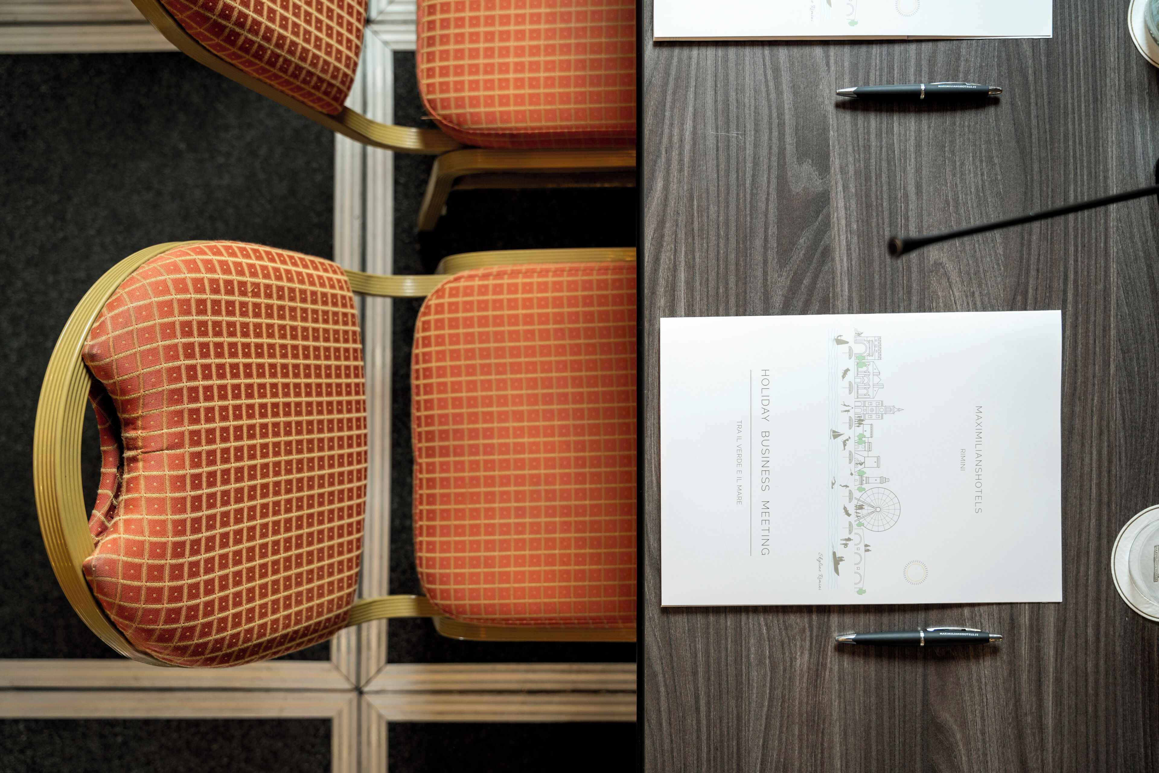 A conference table with a business card, pens, and a chair with a checkered pattern.