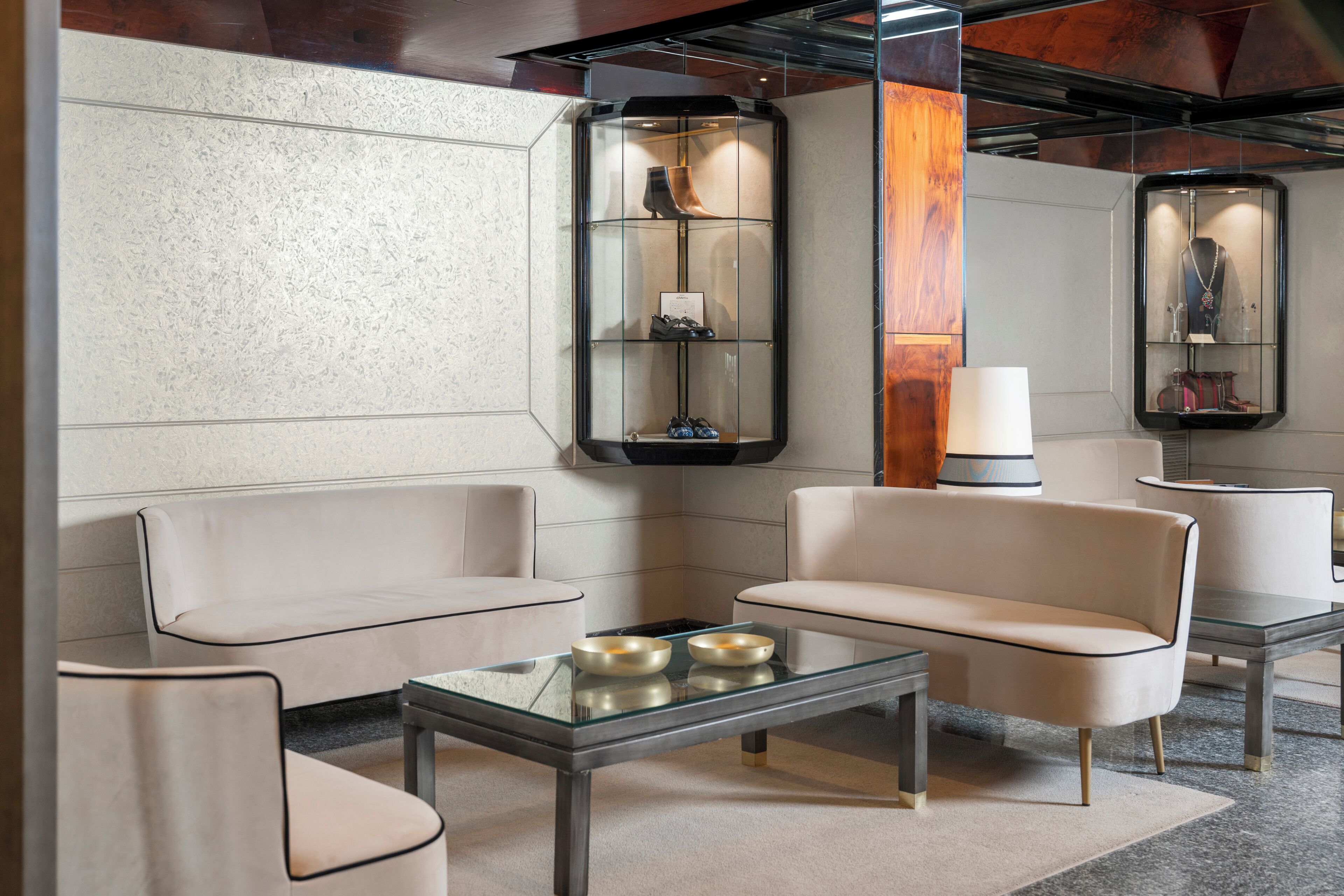 A modern lobby with a glass coffee table, beige sofas, and a shoe display.
