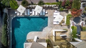Vista aérea de un complejo turístico con piscina, sillas de descanso y un jardín cuidado.