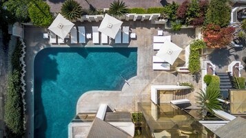 Vista aerea di un resort con piscina, lettini e un giardino curato.