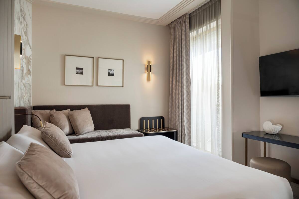A hotel room with a large bed, a desk, a chair, a TV, and two framed pictures on the wall.