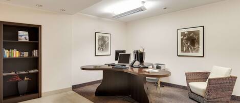 A modern office space with a curved desk, a bookshelf, two framed artworks, and a wicker chair.