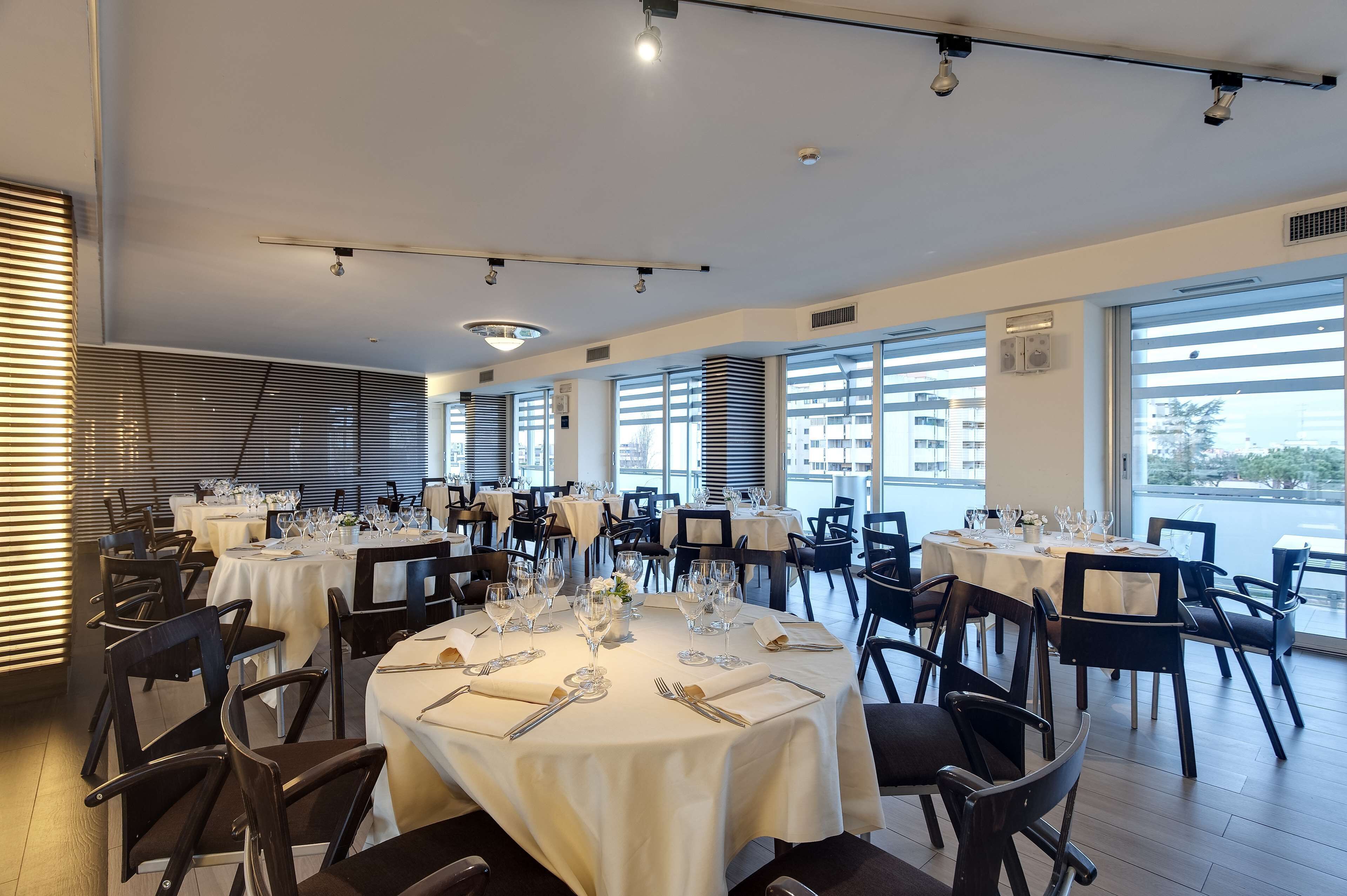 A restaurant with round tables set for dining, large windows, and a view of the city.