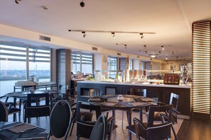 A modern restaurant with a bar area, large windows, and a view of the city skyline. - Occidental Aran Park (Rome)