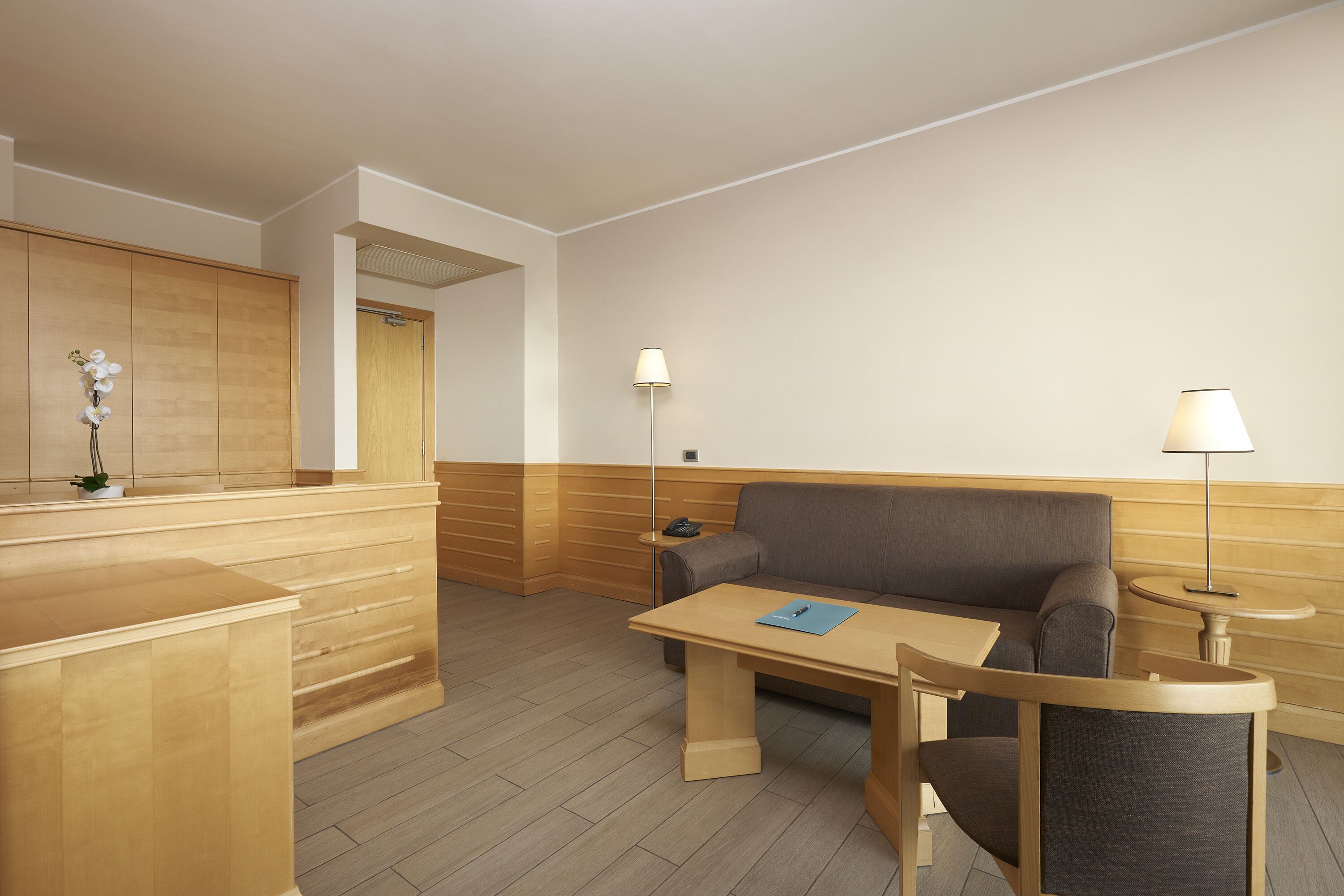 Een moderne hotelkamer met een houten receptiebalie, een bank, een tafeltje en een lamp.