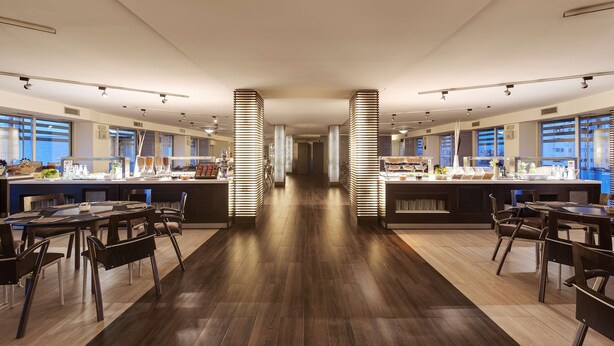 A modern restaurant with a long counter, multiple seating areas, and a central walkway. - Occidental Aran Park (Rome)