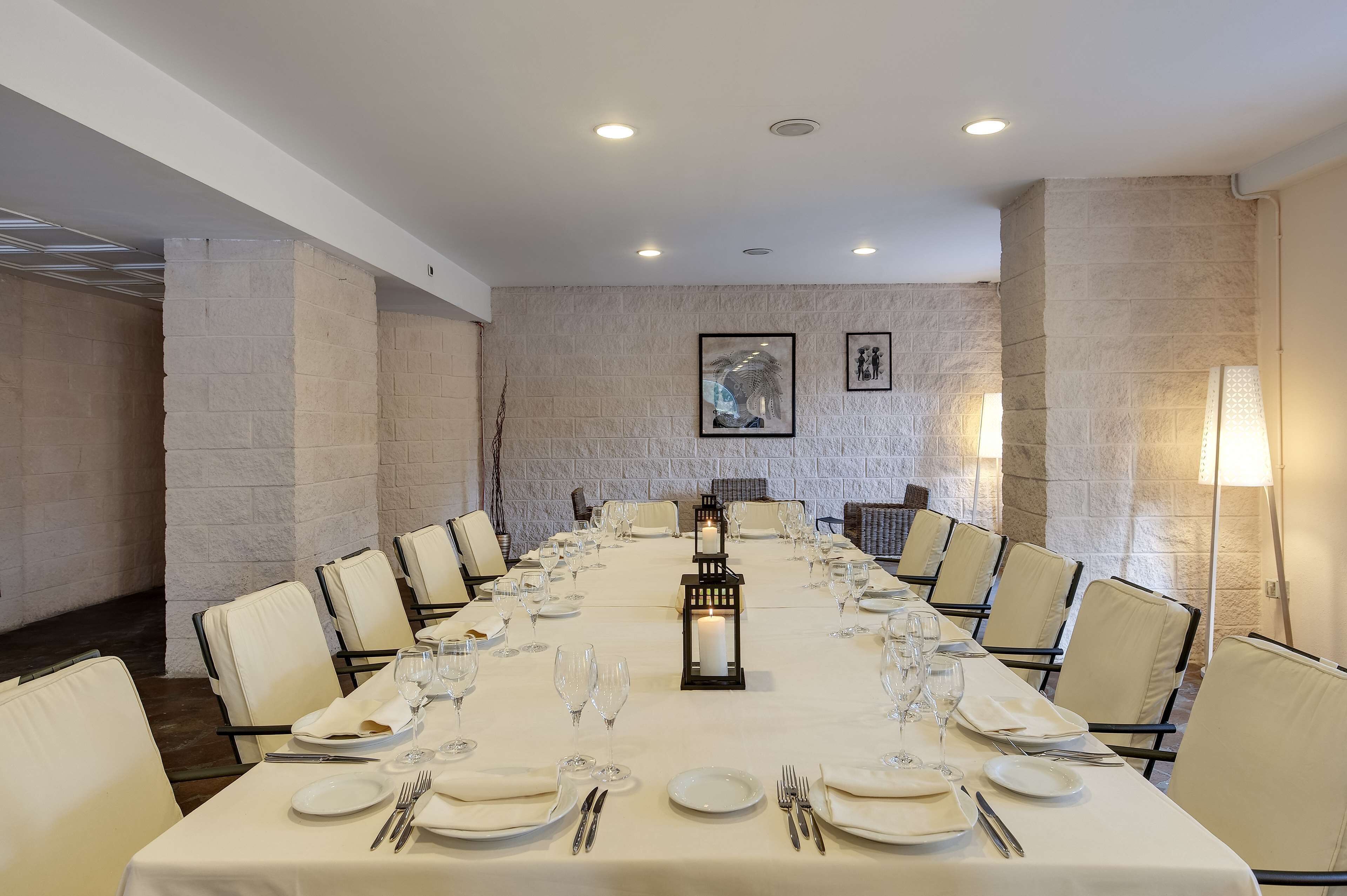 Un salón de conferencias con una larga mesa dispuesta para una reunión, rodeado de sillas, y una vela dentro de un farol en el centro.