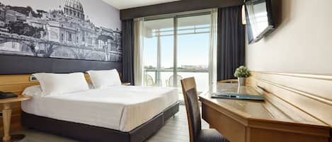 A hotel room with a bed, a desk, a chair, a TV, and a large window with a view.