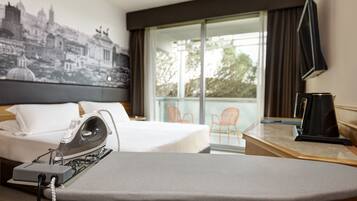 Habitación de hotel con cama, tabla de planchar, televisión de pantalla plana y ventana grande con vista a la ciudad.