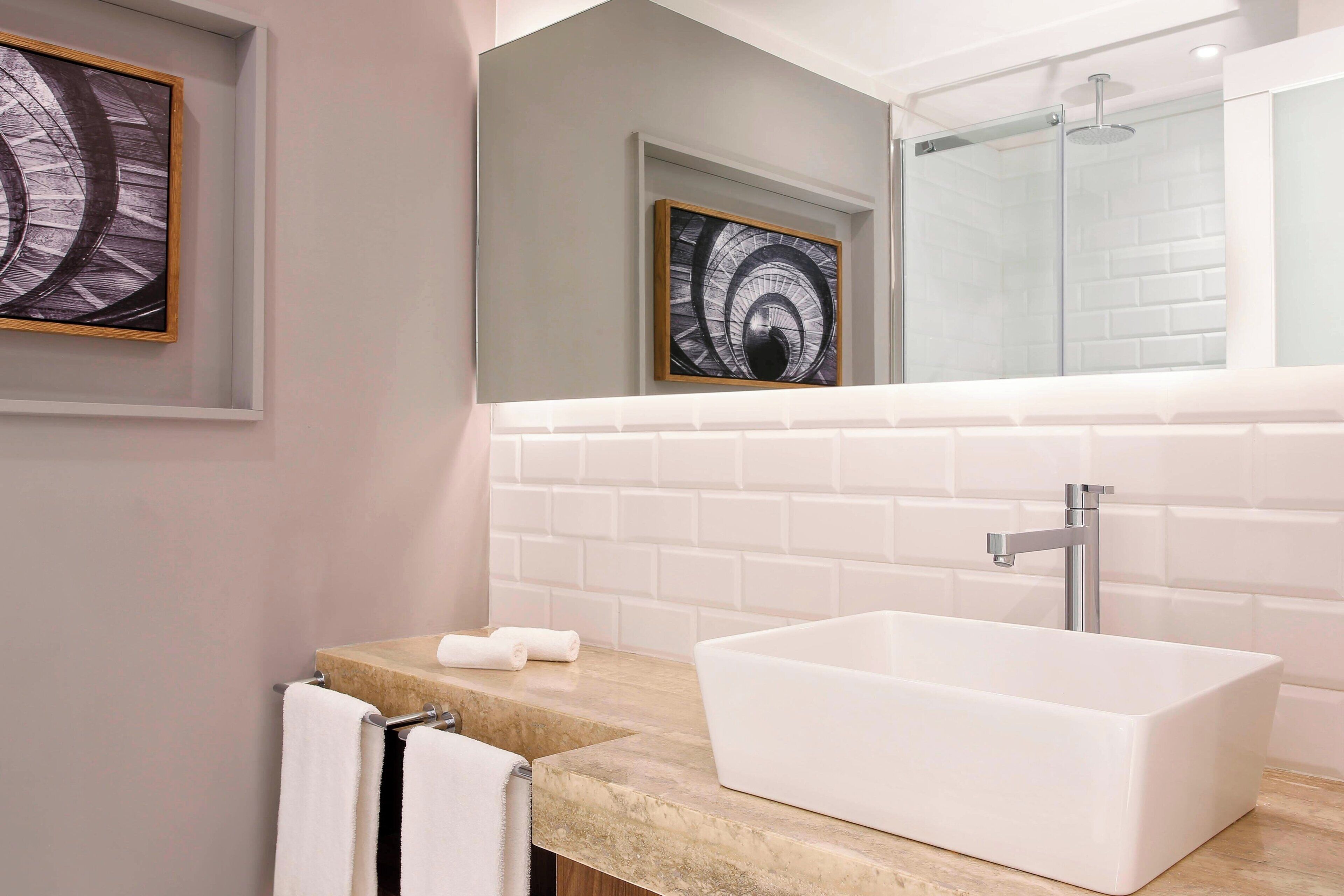 Un baño moderno con un lavamanos rectangular blanco, una cabina de ducha con mampara de cristal y una obra de arte abstracta enmarcada sobre el espejo.
