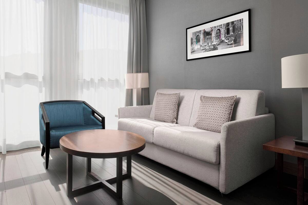 A modern living room with a grey sofa, a blue armchair, a round wooden coffee table, and a framed picture on the wall.