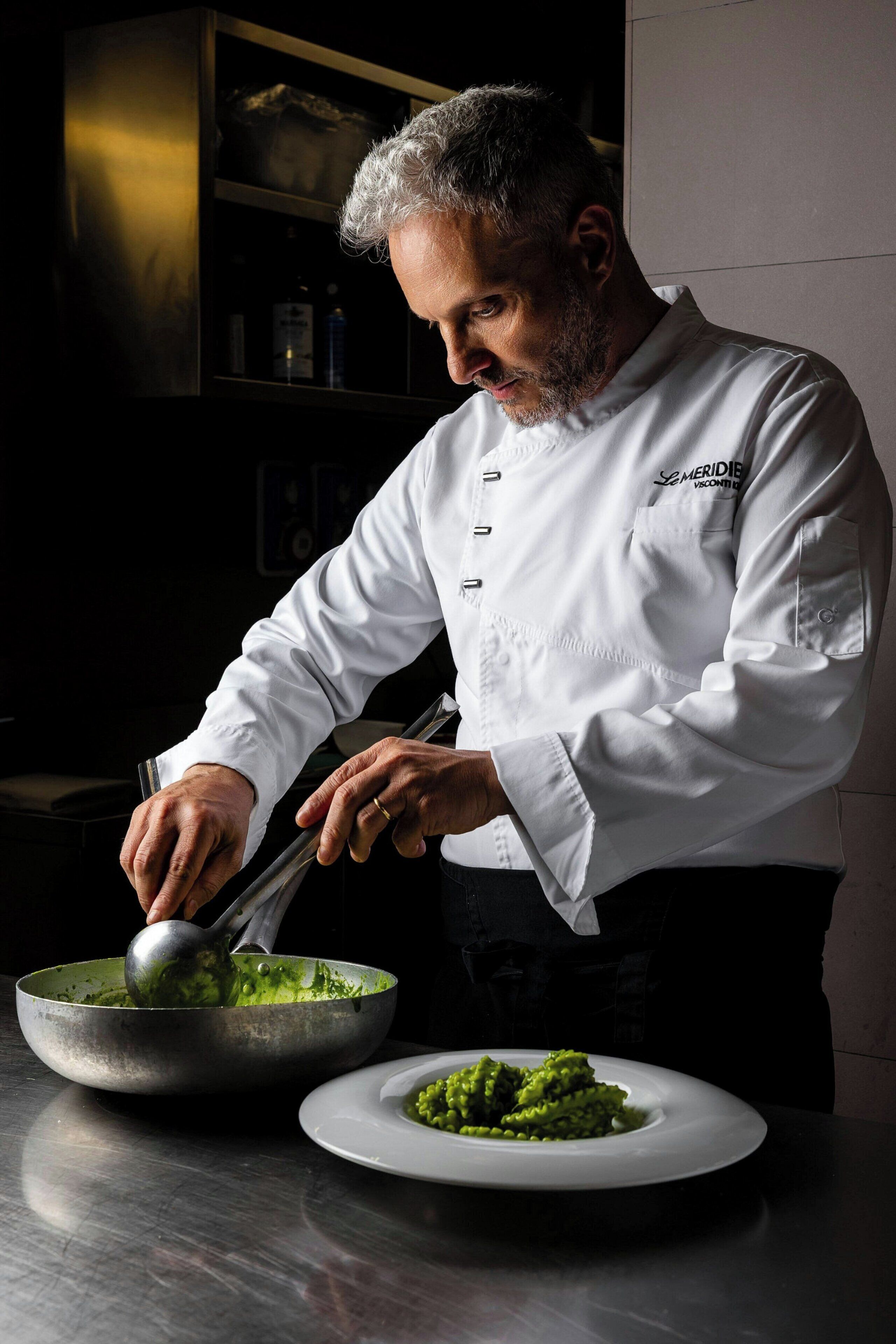 A chef in a white uniform preparing food in a kitchen.