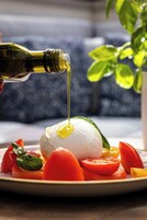 Un piatto con una pallina di formaggio bianco, pomodori e basilico, olio d'oliva che viene versato sopra.