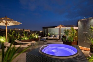 A rooftop patio with a hot tub, lounge chairs, and potted plants.