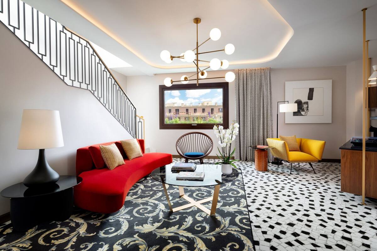 A modern living room with a staircase, a red sofa, a yellow armchair, and a large window with a city view.