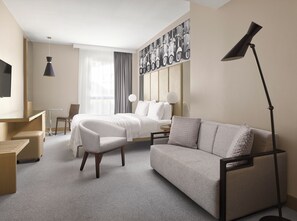 A hotel room with a bed, a sofa, a desk, a chair, a TV, and a lamp.