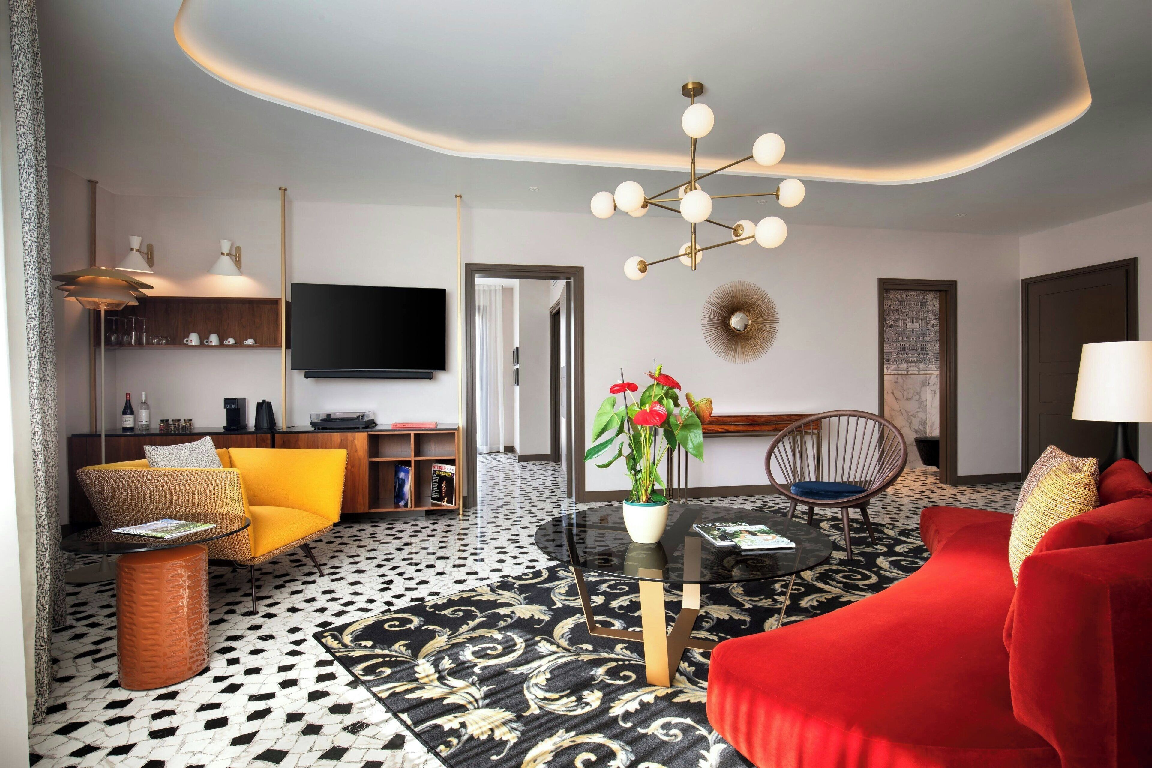 Ein modernes Wohnzimmer mit einem schwarz-weiß gemusterten Boden, einem roten Sofa, einem gelben Sessel, einem Glastisch mit einer Pflanze und einer Deckenleuchte.