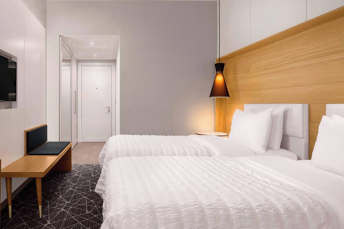 A hotel room with two beds, a desk, a TV, and a lamp.