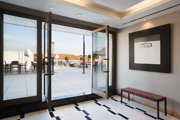 A modern hotel lobby with a glass door entrance, a bench, and a framed picture on the wall.