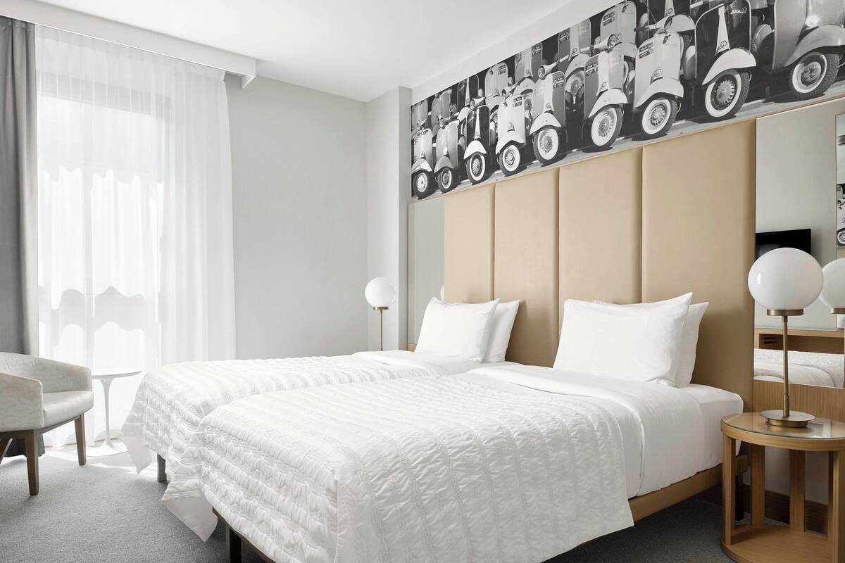 A hotel room with a large bed, a chair, a small table, and a wall-mounted mirror.
