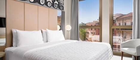 A hotel room with a large bed, a headboard with a cityscape mural, a window with a view of buildings, and a chair.