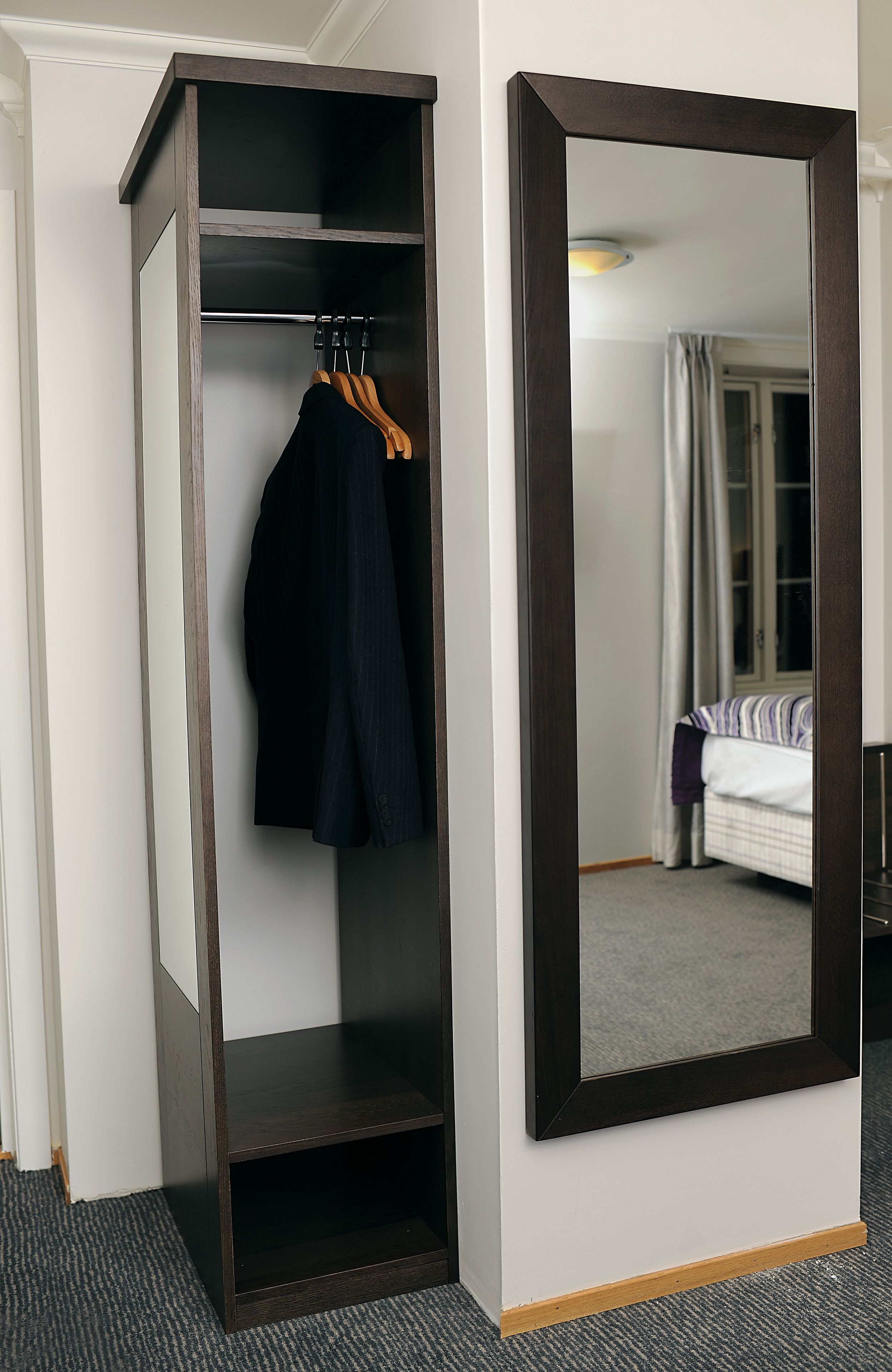 A wardrobe with a mirror, a hanging coat, and a bed in the background.