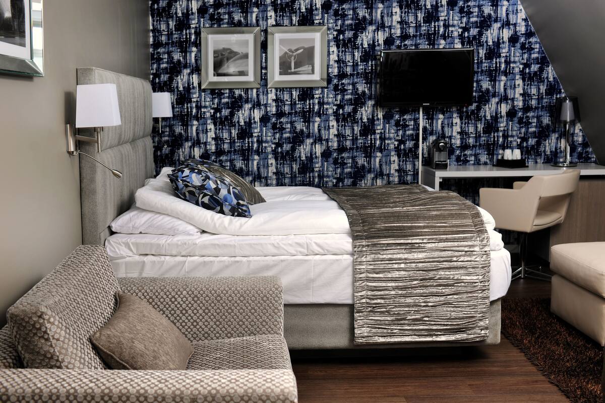 A modern hotel room with a neatly made bed, a desk with a computer, a chair, and a couch.