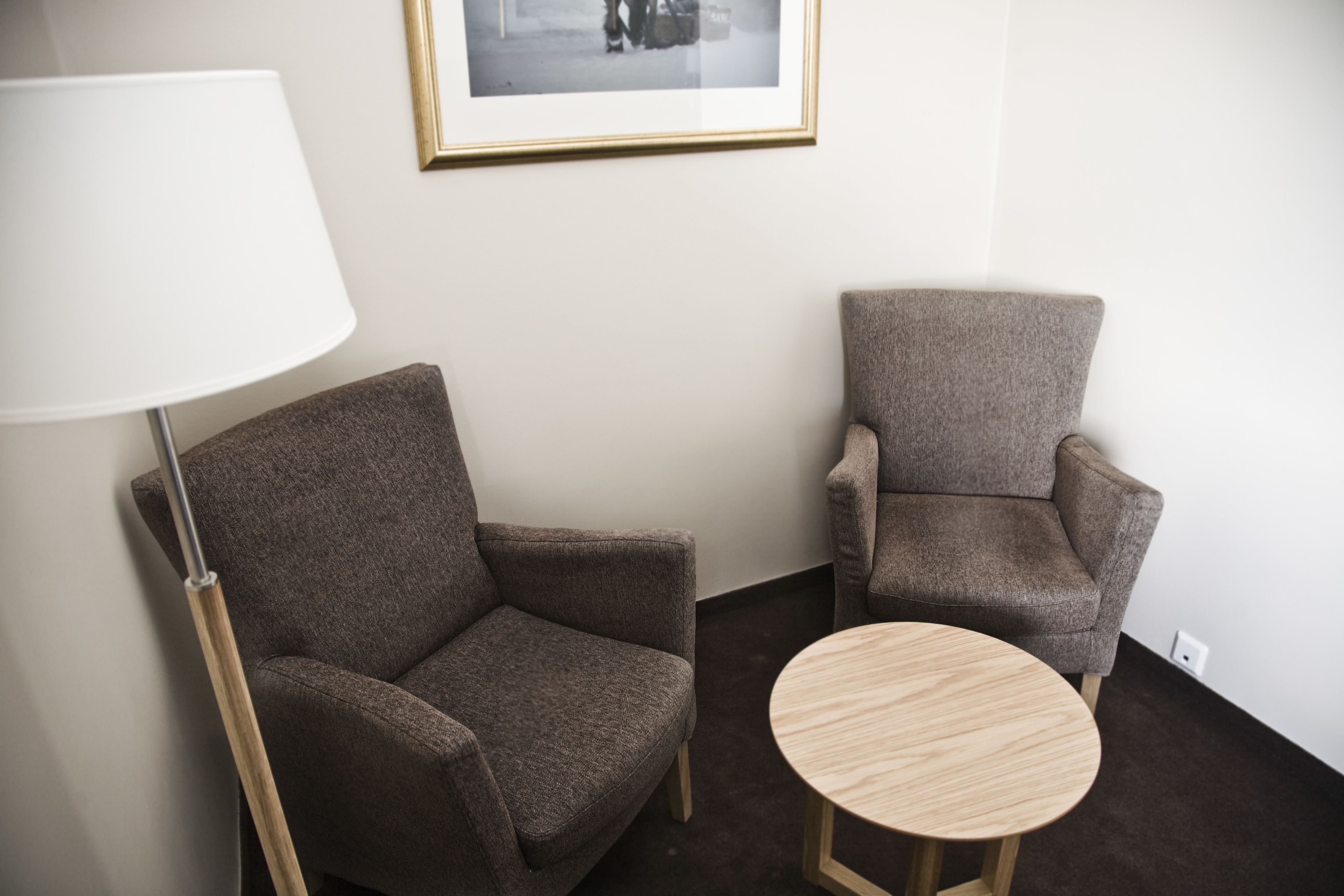 A room with two armchairs, a round wooden table, a floor lamp, and a framed picture on the wall.