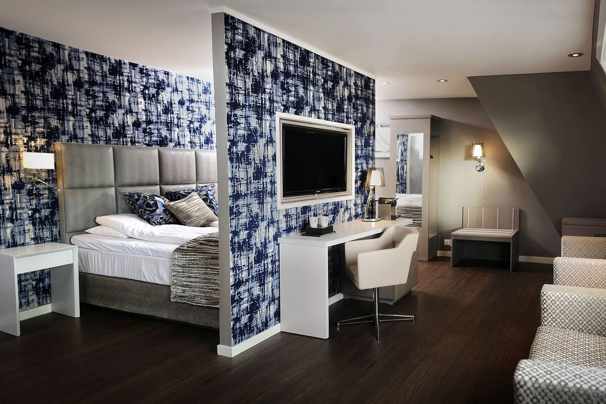 A modern hotel room with a large bed, a desk, a chair, and a TV.