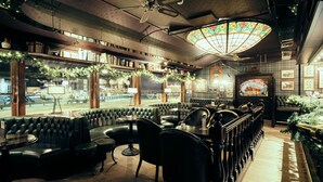 A cozy, well-lit restaurant with a green leather booth seating area, a large stained glass window, and a view of the street outside. - Bergstadens Hotel & SPA (Roros)