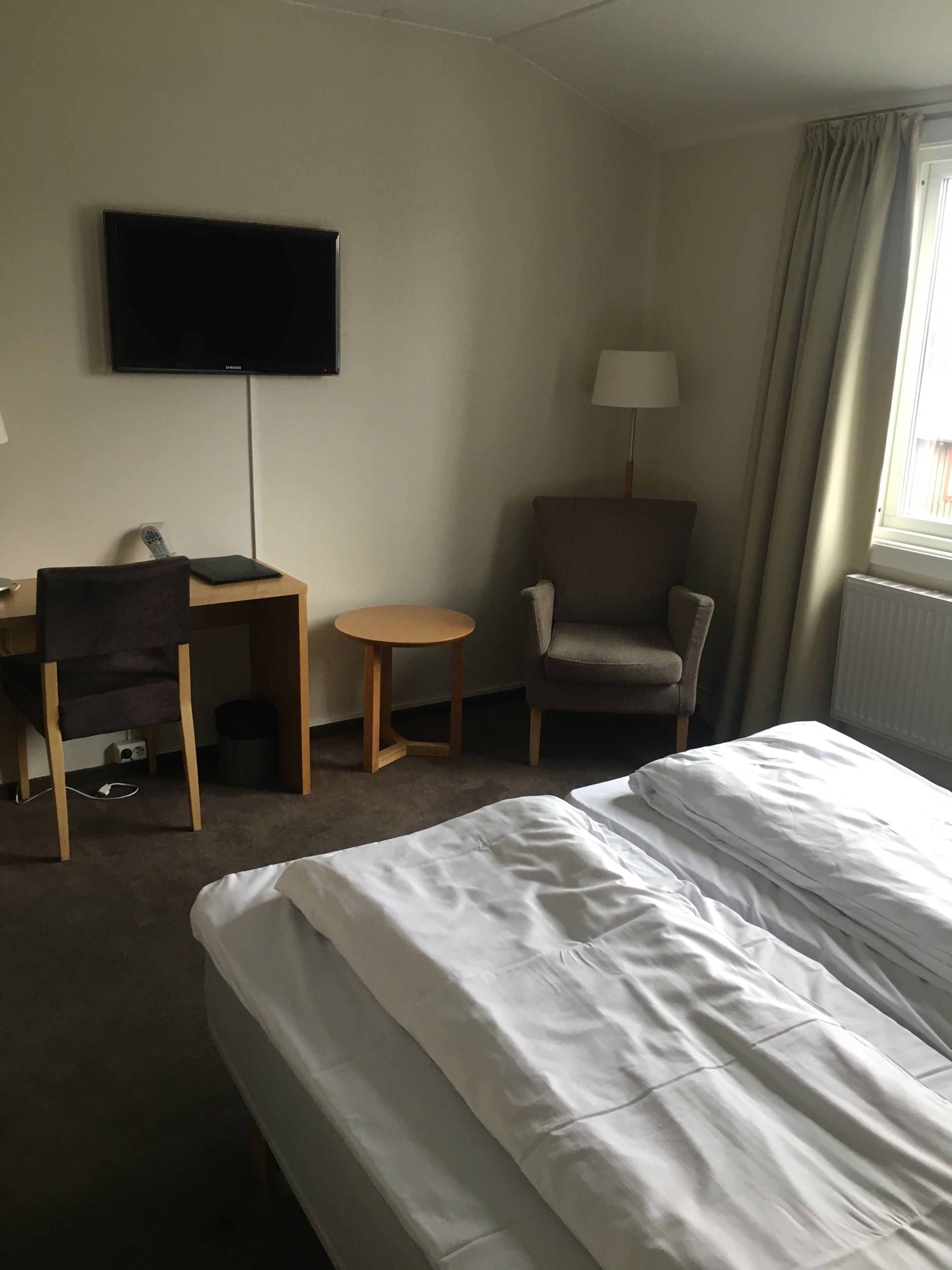A hotel room with a bed, a desk, a chair, a television, and a lamp.