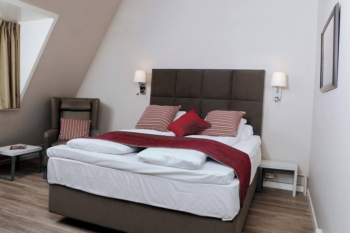 A modern bedroom with a large bed, a chair, bedside tables, and a window with curtains.
