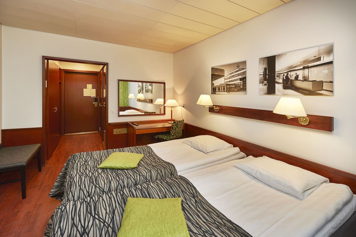 Habitación de hotel con dos camas, un banco, un escritorio y un espejo.
