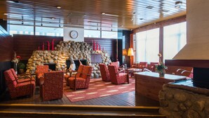 Un hall d’entrée accueillant, doté d’une cheminée en pierre, de fauteuils à motifs rouges et d’un plafond en bois.