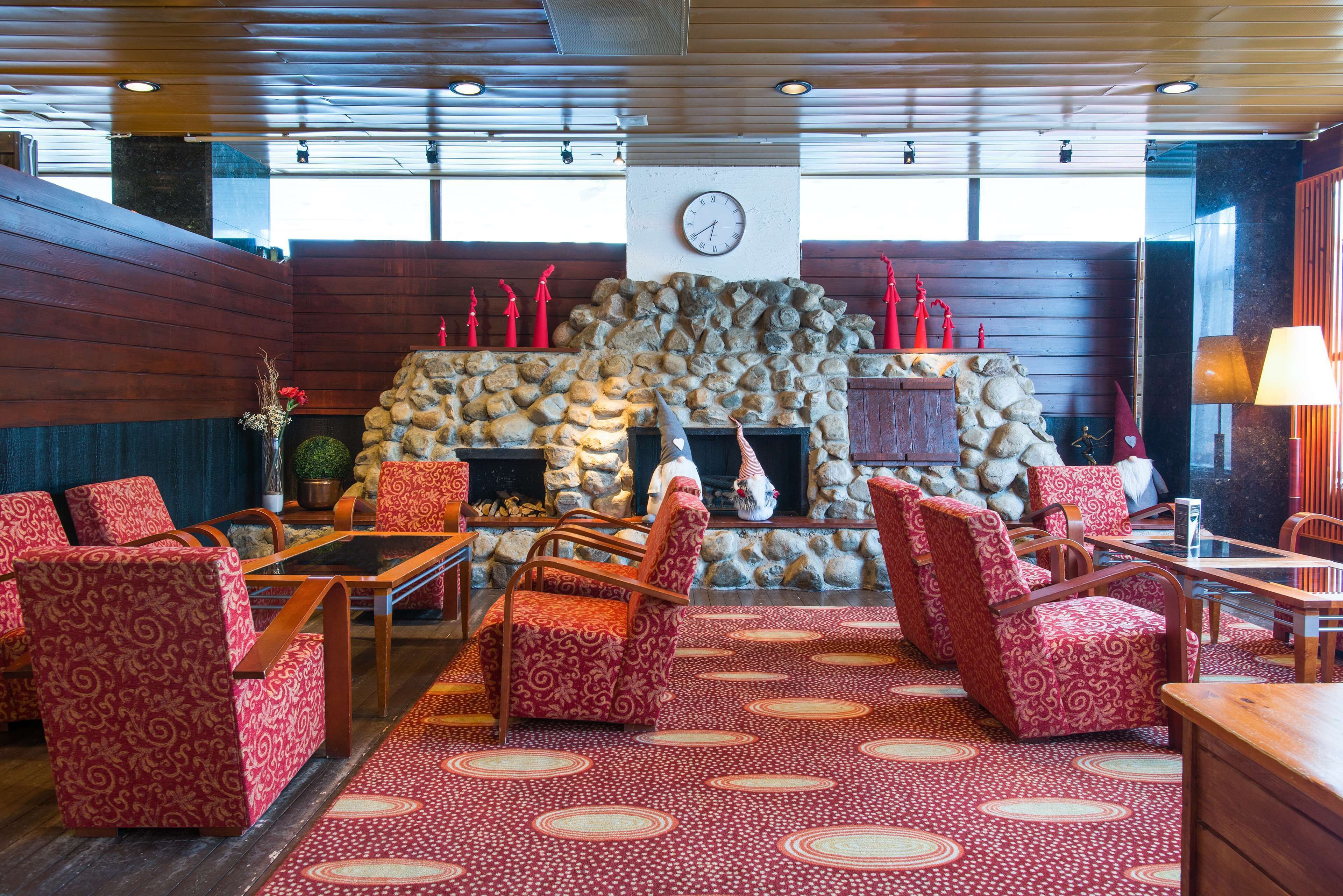 A cozy lobby with a stone fireplace, red patterned chairs, and a wooden ceiling.