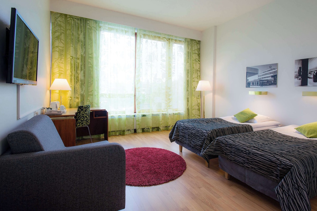 Una habitación de hotel con dos camas, televisión, escritorio y una alfombra roja.