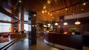 Un hall d’hôtel moderne avec un plafond en bois, un comptoir d’accueil, un espace salon et une grande fenêtre.