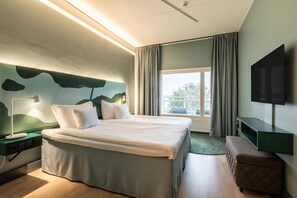 A modern hotel room with a large bed, a flat-screen TV, a nightstand, and a view of the outdoors.
