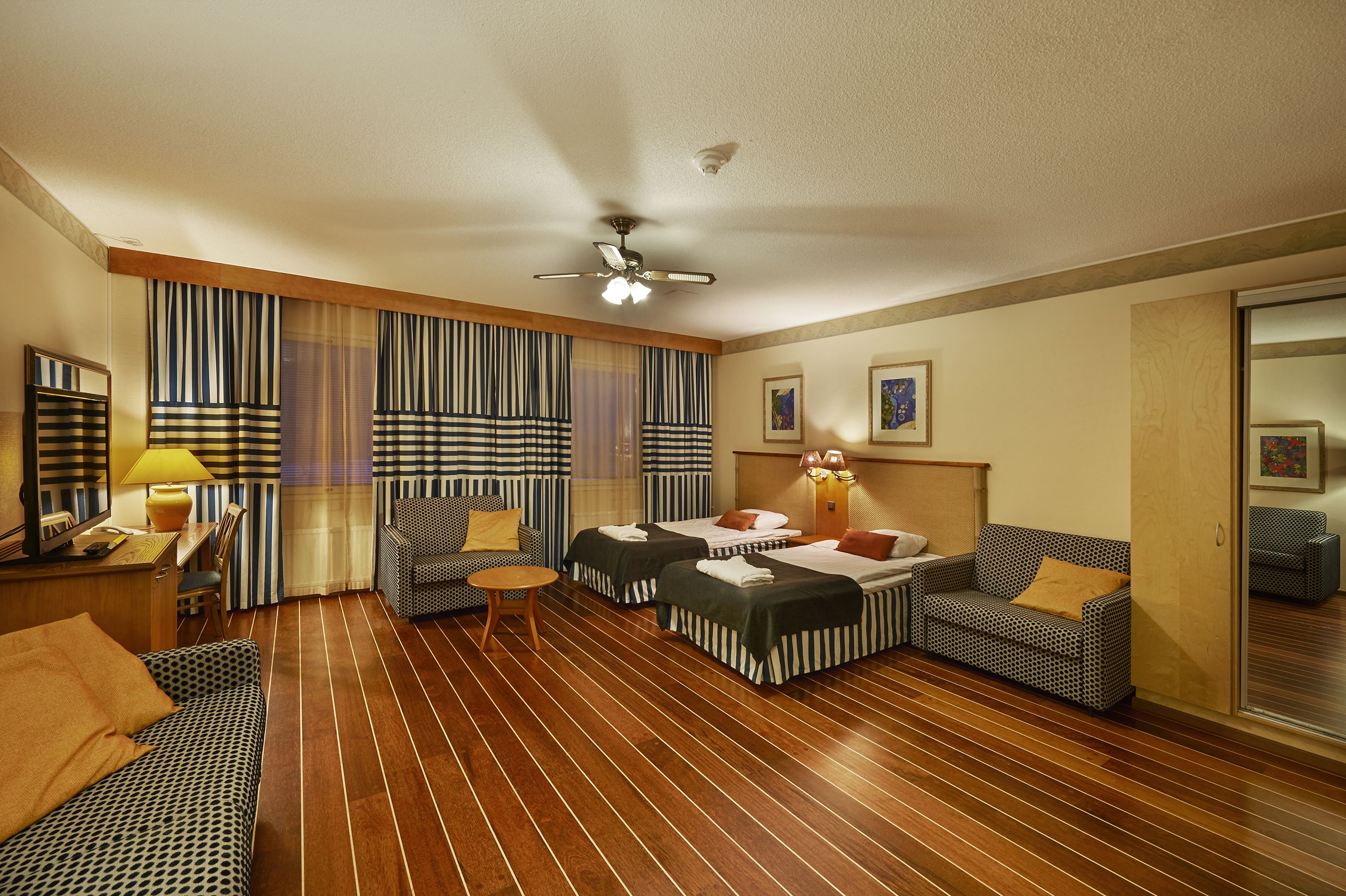 Habitación de hotel con dos camas, un sofá, una silla, una mesita y un ventilador de techo.
