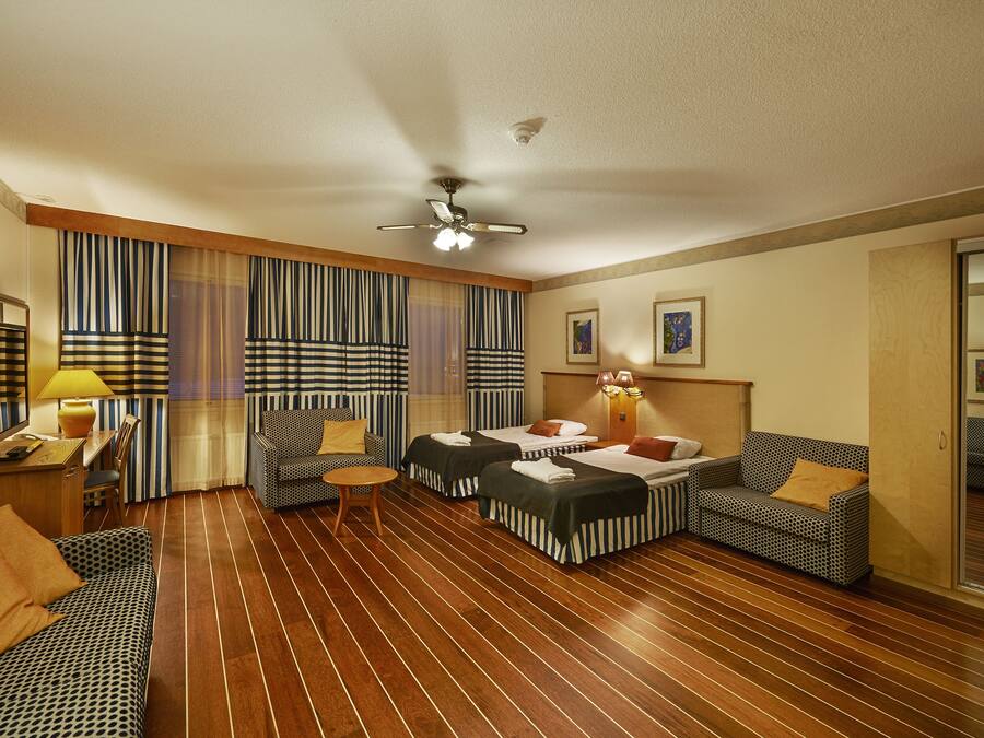 Habitación de hotel con dos camas, un sofá, una silla, una mesita y un ventilador de techo.