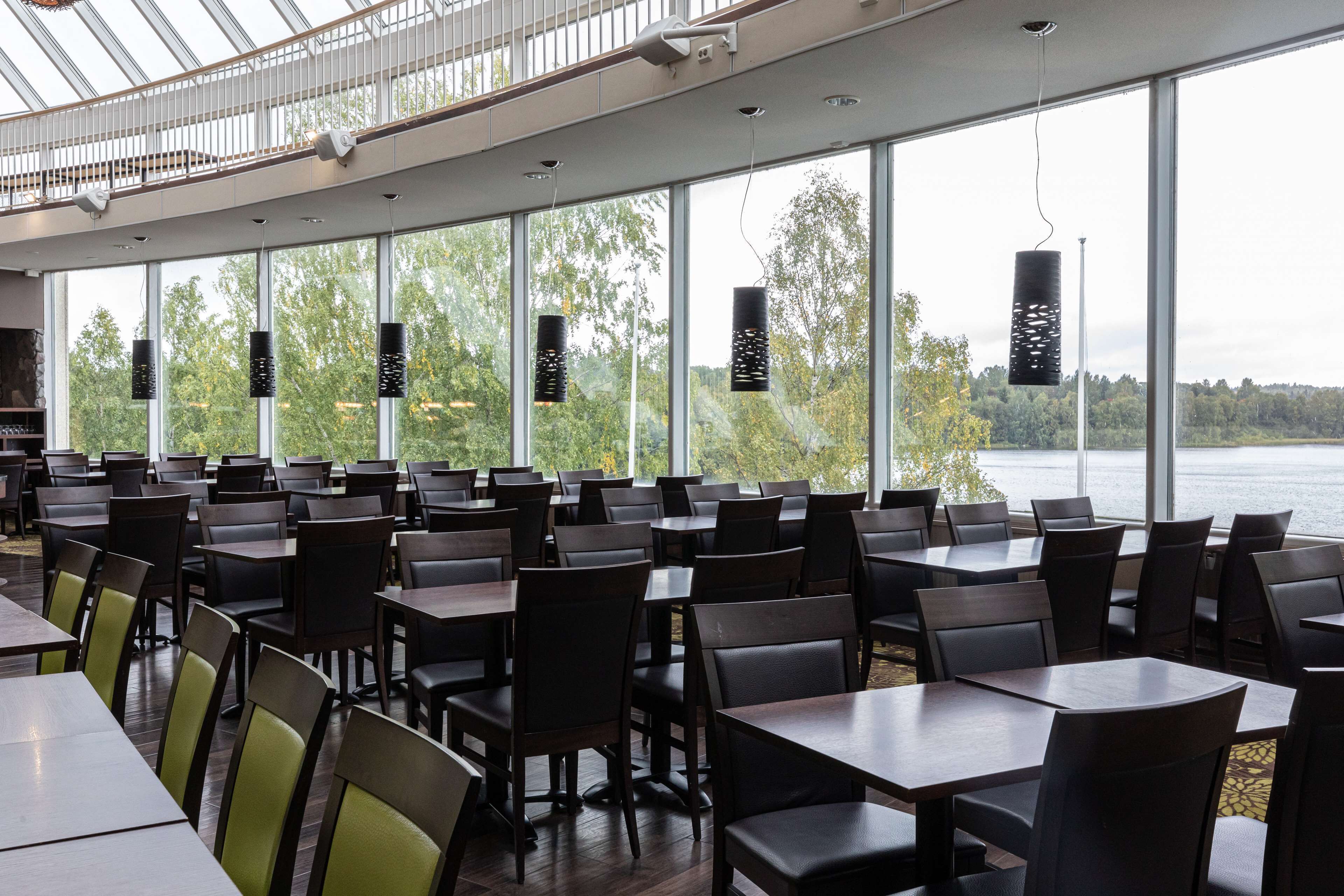 Tilava ravintola, jossa on suuret ikkunat, joista avautuu näkymä järvelle ja puustoon.